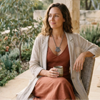 Woman sitting outdoors holding a cup, surrounded by nature