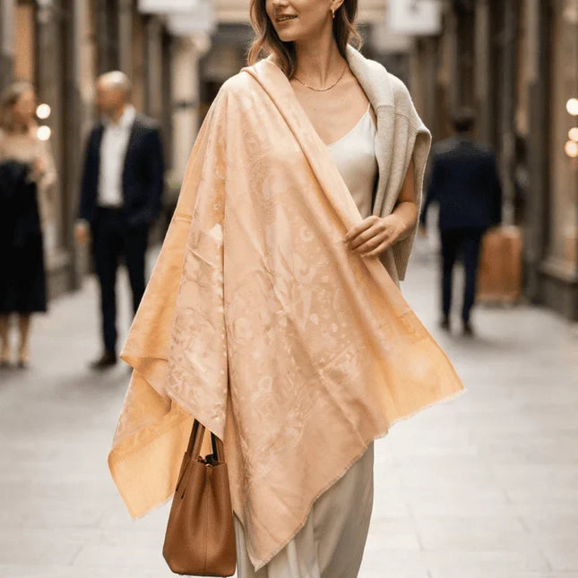 Woman walking down a street wearing a beige shawl and holding a brown bag.