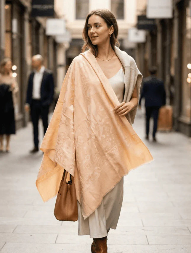 Woman walking down a street wearing a beige shawl and holding a brown bag.