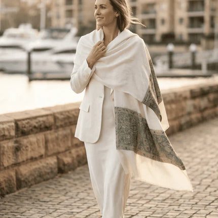 Woman in a white outfit with a shawl walking along a waterfront promenade.
