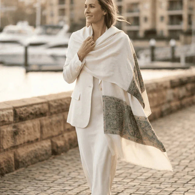 Woman in a white outfit with a shawl walking along a waterfront promenade.