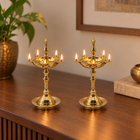 Two brass nilavilakku lamps with lit jyotis, displayed on a polished wooden table in a warm indoor setting.