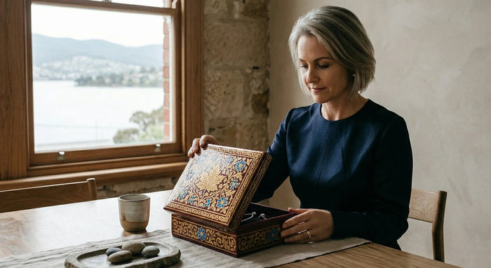 Woman opening a decorative box at a table with a scenic view outside the window.