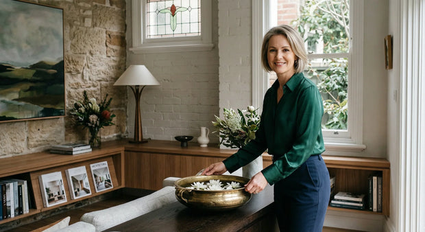 Woman in a green sweater standing in a room with a wooden table and decorative items.