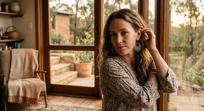 Woman standing in a room with large windows, looking out onto a garden.